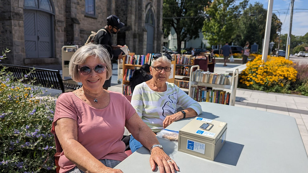 Two women at a Friends of the Library outdoor book sale, one smiling