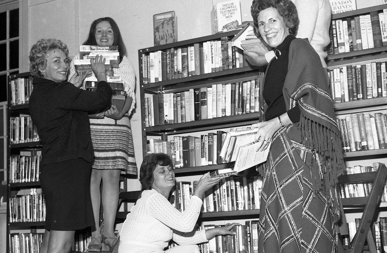 Black and white photograph of five women holding books in front of library stacks