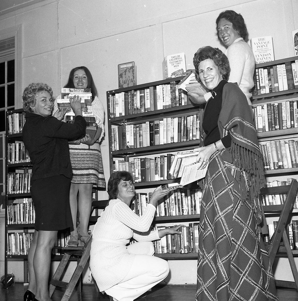 Women organizing books on shelves in a vintage library.