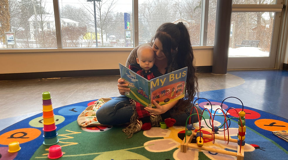 Woman reading 'My Bus' book to a baby on a colorful playmat