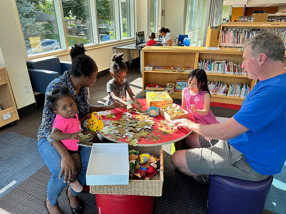 Children and adults playing with puzzles and toys at a low table in a library.