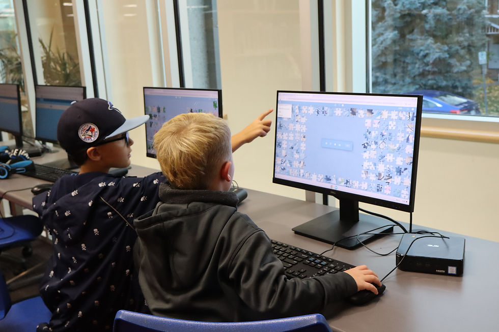 Two children sitting at a computer desk playing a game.