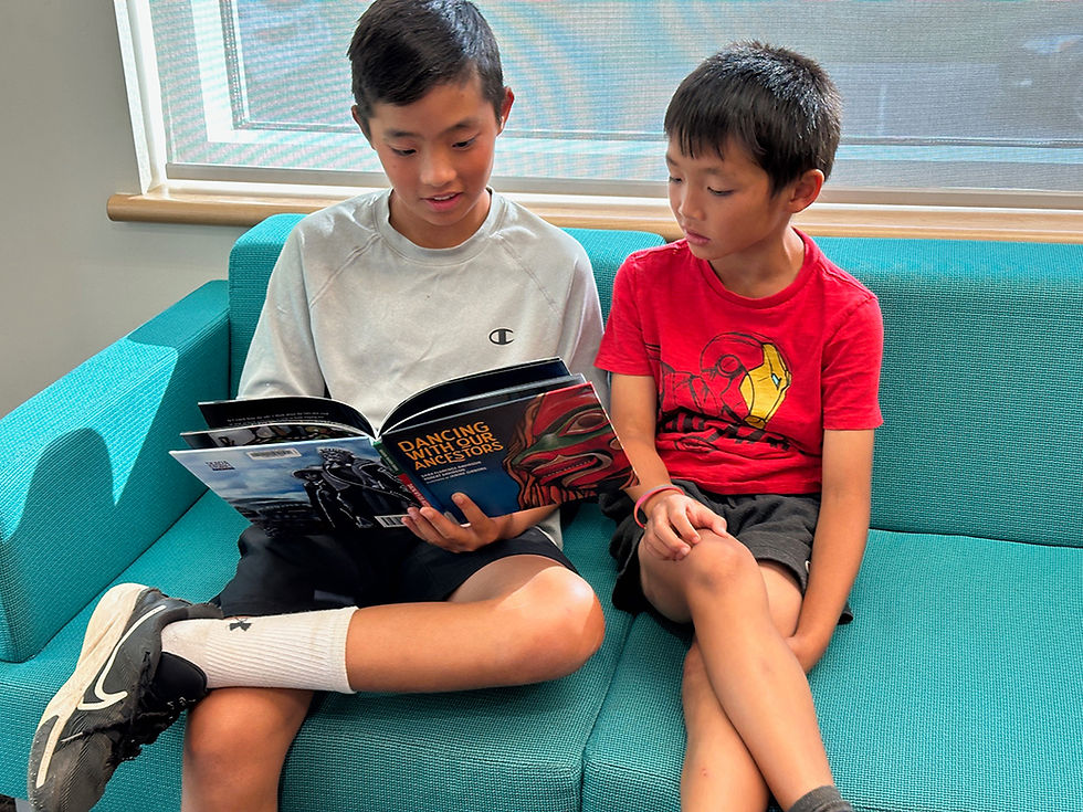 Two boys sitting on a teal sofa reading a book.