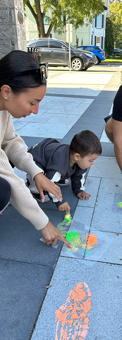 A child and an adult are using colourful chalk on a paved outdoor area.