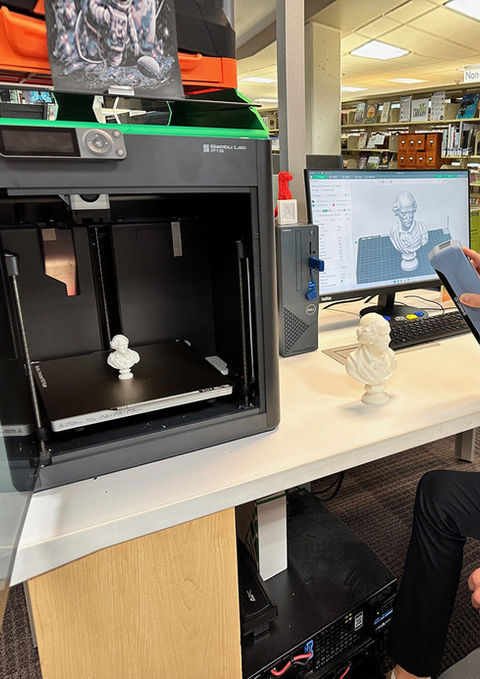 Person using a 3D scanner near a 3D printer in a library.