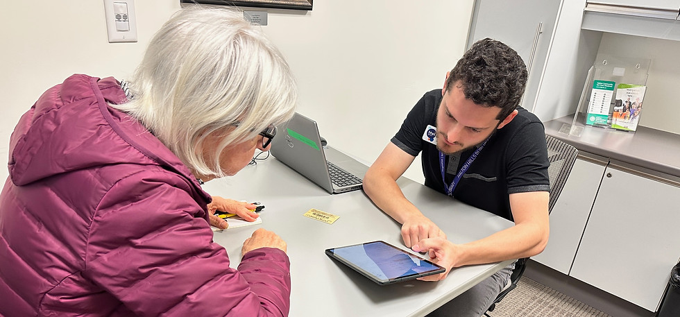 A staff member assists a patron with a tablet at a desk.