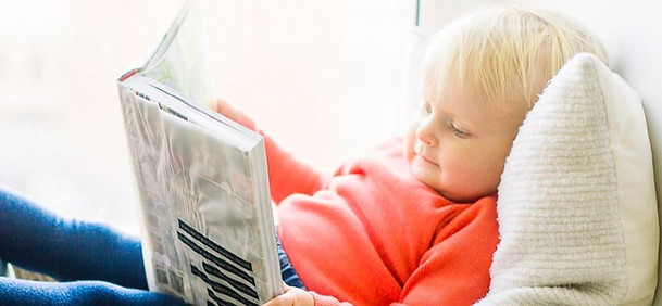 A young child reclining and reading a book.