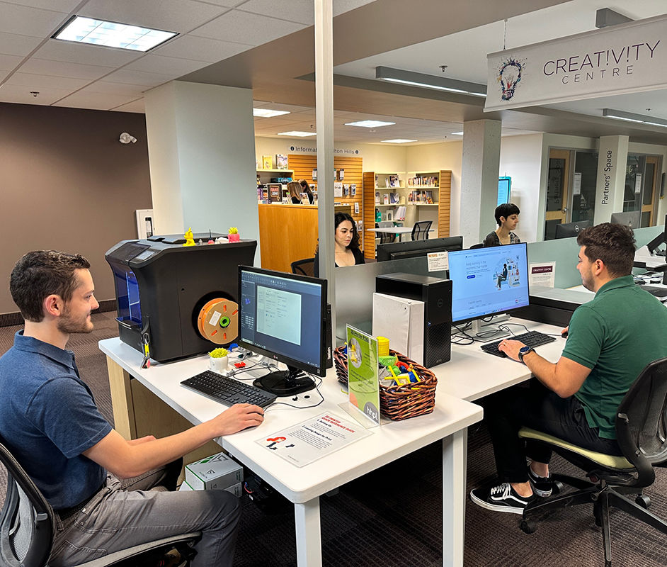 People using computers and equipment in a library technology centre.