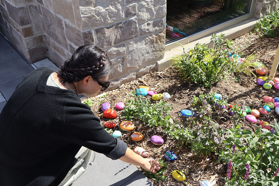 Woman placing colorful painted rocks in a garden.