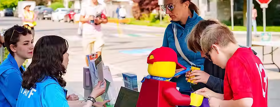 Kids and an adult working on a LEGO robot outdoors with a laptop.