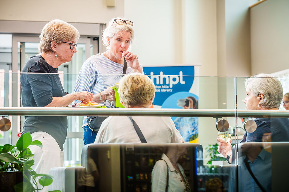 Older women interacting at an event with an 'hhpl' sign
