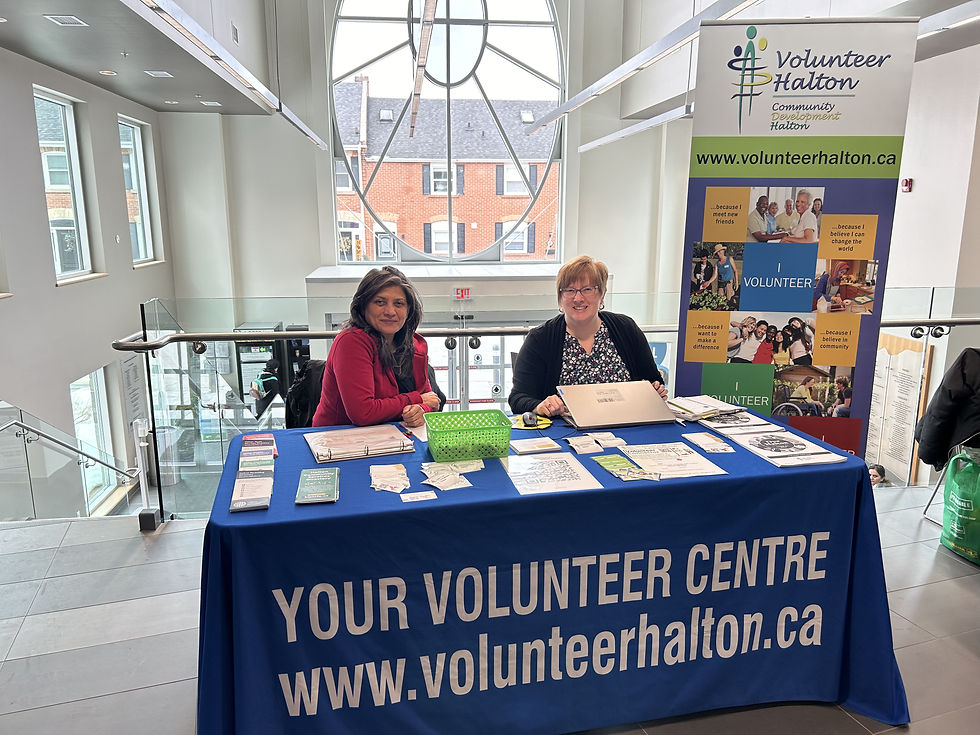 Two women at a volunteer information table with brochures and a banner indoors.