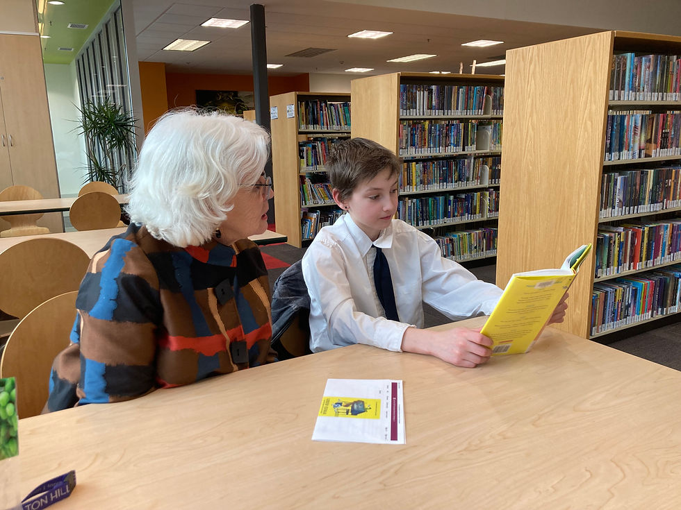 A child and an older adult sitting at a table reading a book together.