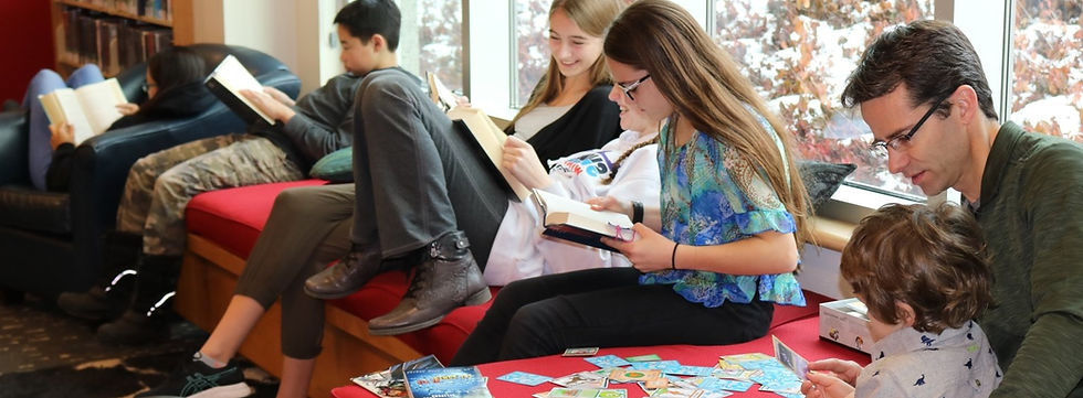 6 people sit on a bench next to a window reading books and playing with cards.